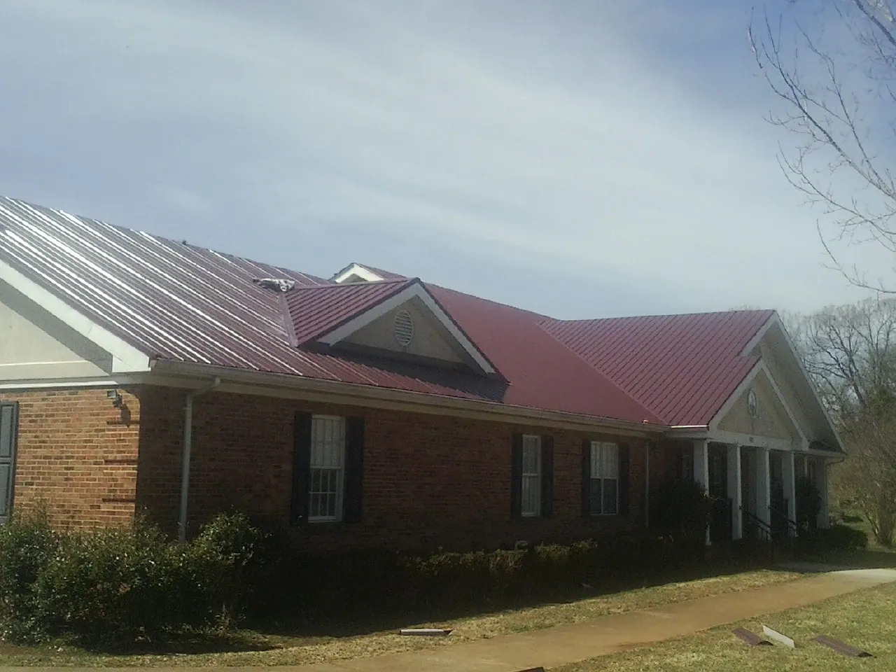 Red metal roof with gabled entries on a long brick building, from a Hail Damage Roof Repair job in Trenton